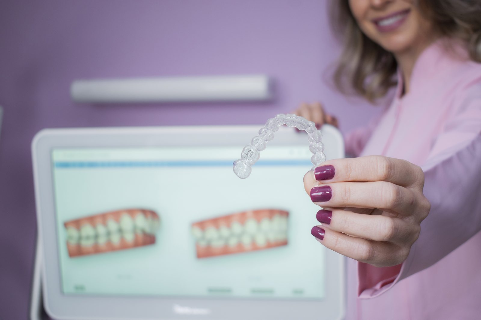 Dra. Gabriela Cavalheiro segurando alinhador Invisalign, simulação de sorriso ao fundo